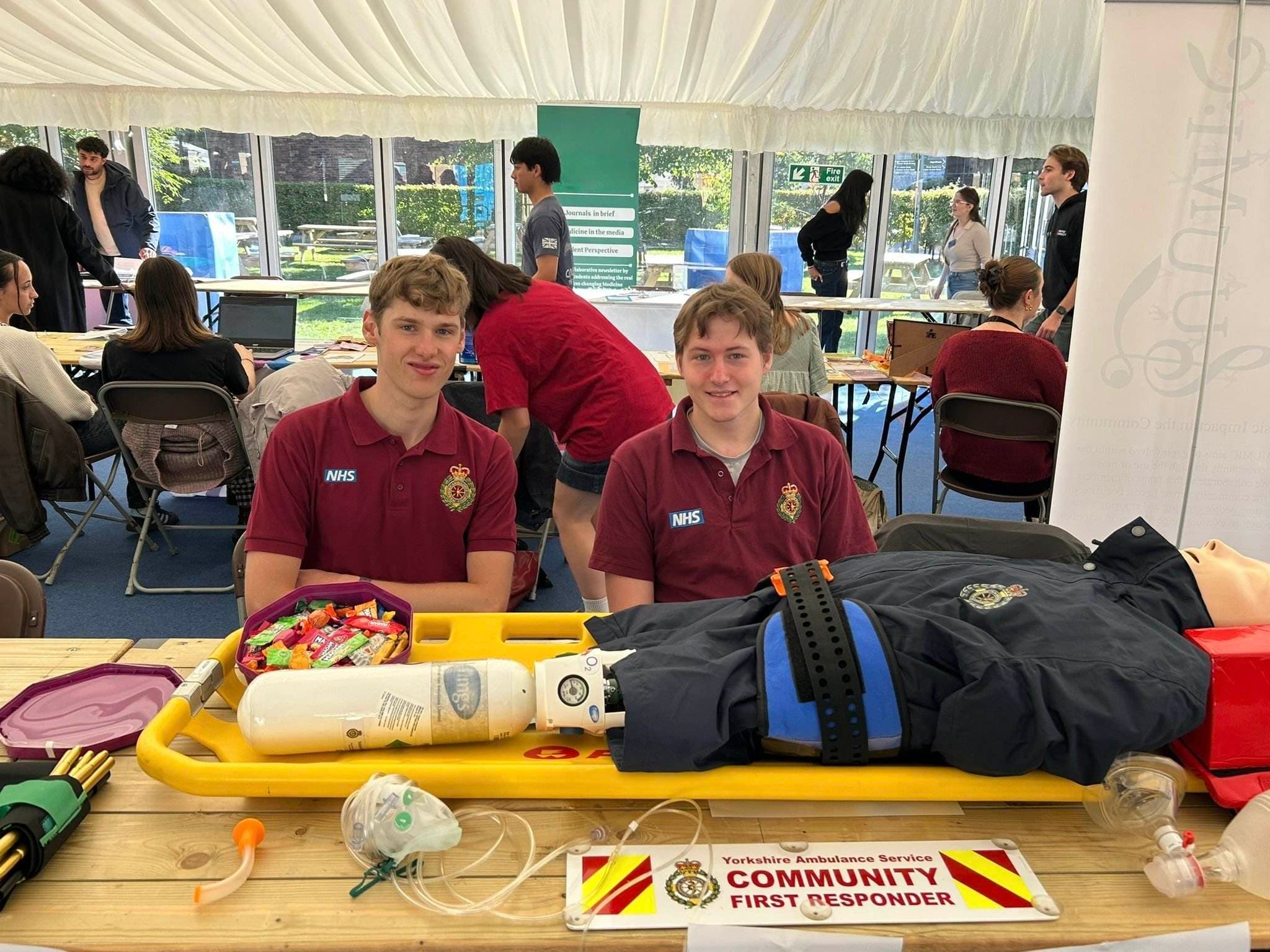 Cam and Rory at the LSCFR stall with full equipment display including CPR mannequin, oxygen, and CFR banner
